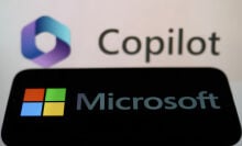 Microsoft logo displayed on a phone screen and Copilot displayed on a screen in the background.