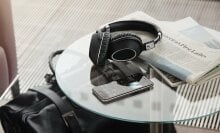 a pair of sennheiser headphones sitting next to a phone and a pile of newspapers on a glass table