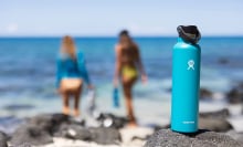 Blue water bottle on rocks wit two people on beach walking away out of focus in background