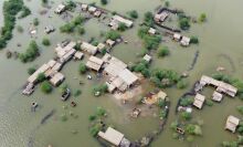 An aerial shot of a flooded residential area. The roofs of houses and the very tops of trees poke out from a green body of water.