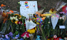 Several bouquets of flowers and stuffed animals rest on the ground on top of a handmade sign that reads "Love will win". 