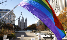 A rainbow flag waves in the air in front a Mormon temple.