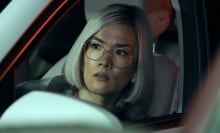 Ali Wong, wearing glasses and sporting a blonde bob, sits in a car looking concerned.