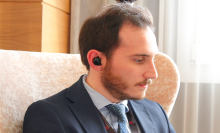 man is sitting down, looking to his left, with translator earbuds in his right ear 
