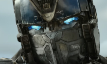 A close-up of the face of a giant metal robot with glowing blue eyes.