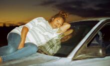 A pregnant woman lies on a car hood and window.