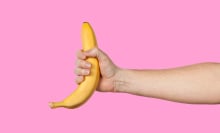 An outstretched arm holds a banana on a pink background