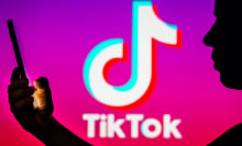 A person's silhouette holds a smartphone with the TikTok logo in the background.
