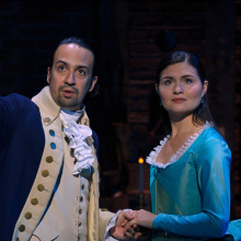 Two people in period garb stand on stage in a production of "Hamilton."