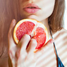 An image of a woman with her fingers in a citrus fruit.