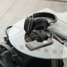 a pair of sennheiser headphones sitting next to a phone and a pile of newspapers on a glass table