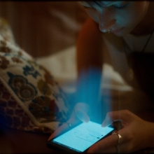 A young adult looks over their phone, which is emitting a strong light toward them. 