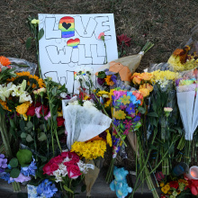 Several bouquets of flowers and stuffed animals rest on the ground on top of a handmade sign that reads "Love will win". 