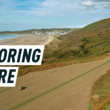 A tractor sows over plain land near the coast in Devon. Caption reads: restoring nature