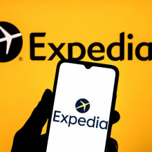 Expedia logo on a smartphone against the backdrop of the Expedia logo on a large screen