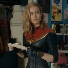 Captain Marvel stands in a teen bedroom covered in fandom for Captain Marvel.