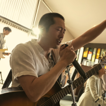 Steven Yeun sings into a microphone fronting a church band and raising his arm in praise in "Beef."