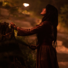 A woman holds her bloody hand out over an alter at night. 