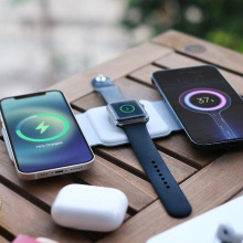 foldable charging station is laid out on a wooden table, with two iphones and a smartwatch being powered up