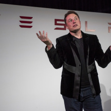 Elon Musk in front of Tesla logo