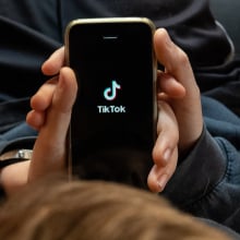 Someone holding an iPhone showing the TikTok logo in their lap. 