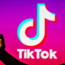 A person's silhouette holds a smartphone with the TikTok logo in the background.