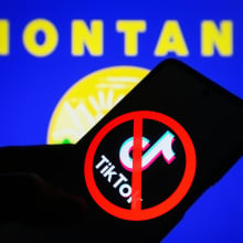 A crossed-out TikTok logo is seen on a smartphone and flag of the state of Montana on a pc screen.