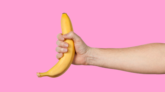 An outstretched arm holds a banana on a pink background