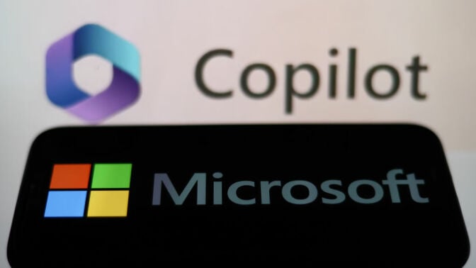 Microsoft logo displayed on a phone screen and Copilot displayed on a screen in the background.