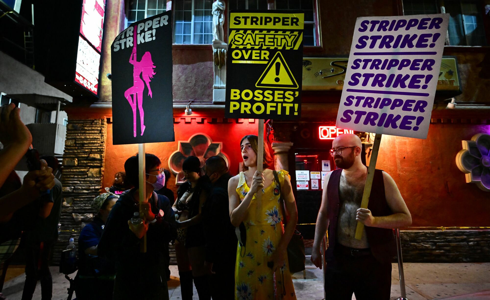 Three people join the stripper strike holding picket signs that read "stripper strike!" and "stripper safety over bosses' profit".