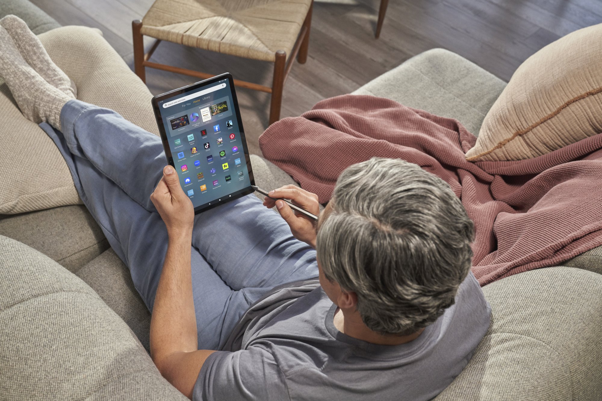 an overhead view of a man using the amazon fire 11 max tablet with its stylus while sitting on a tan couch