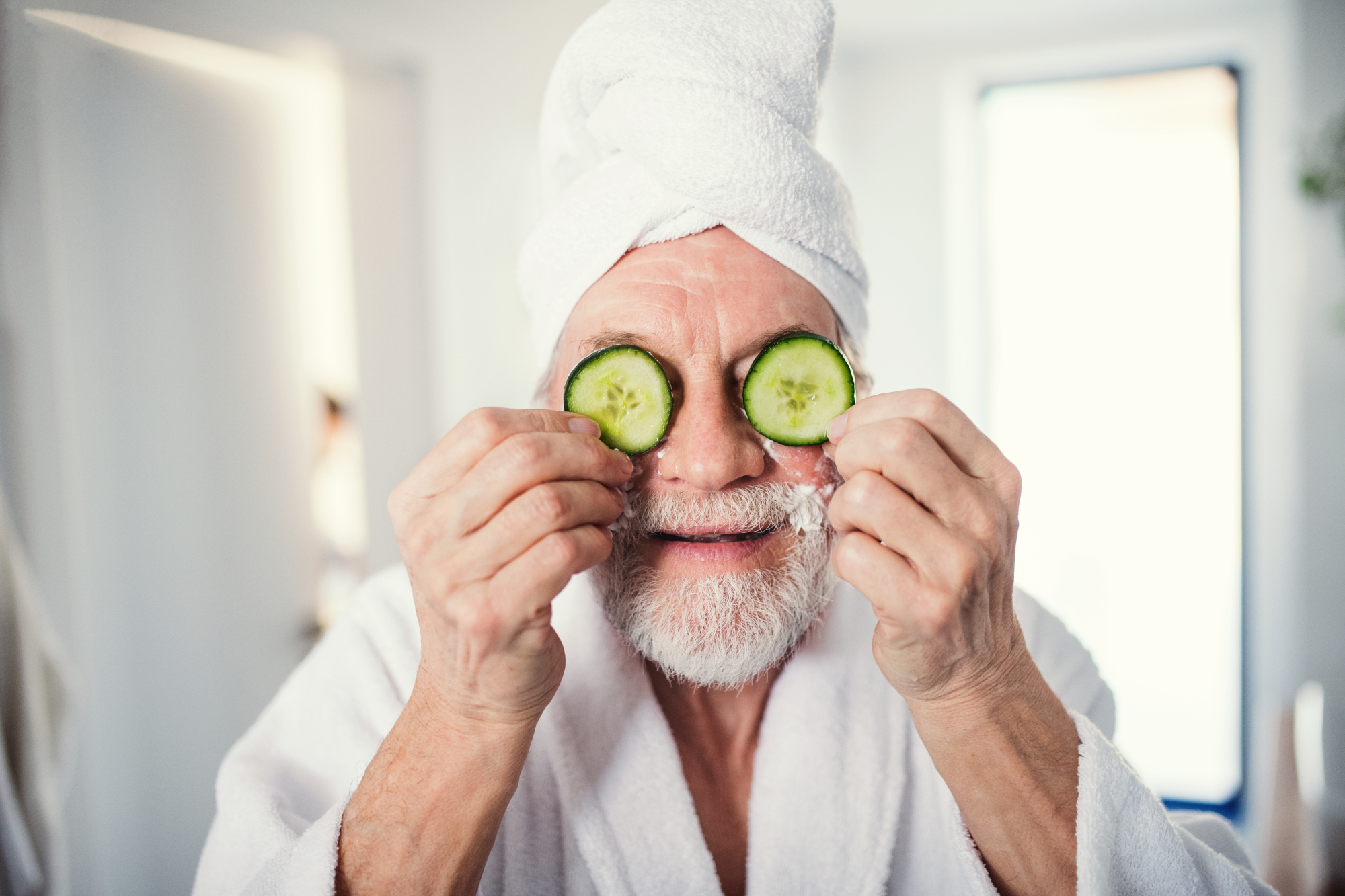 a middle-aged man holding cucumbers over his eyes