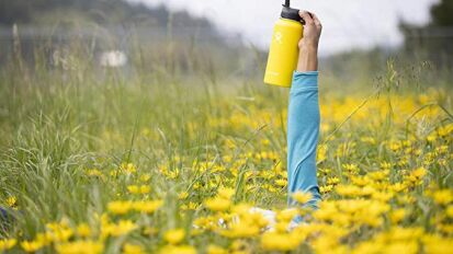 Person holding a yellow Hydro Flask water bottle in a field.