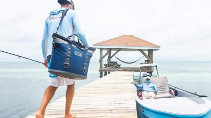 Person carrying the YETI Hopper M30 portable soft cooler on a dock.