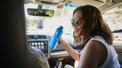 Person sitting in front seat of car and holding Hydro Flask water bottle