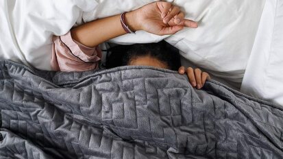a person snuggling under a gray Gravity Blanket