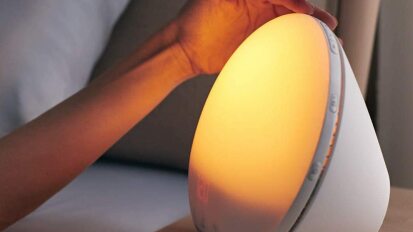 The Philips SmartSleep Wake-Up Light on a bedside table with a hand above it