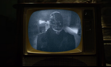 A television screen displays a man wearing a creepy mask. 