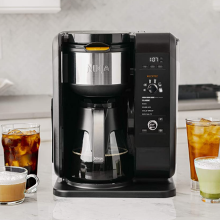 Ninja coffeemaker on a table, four cups of coffee and tea on each side set up on a countertop