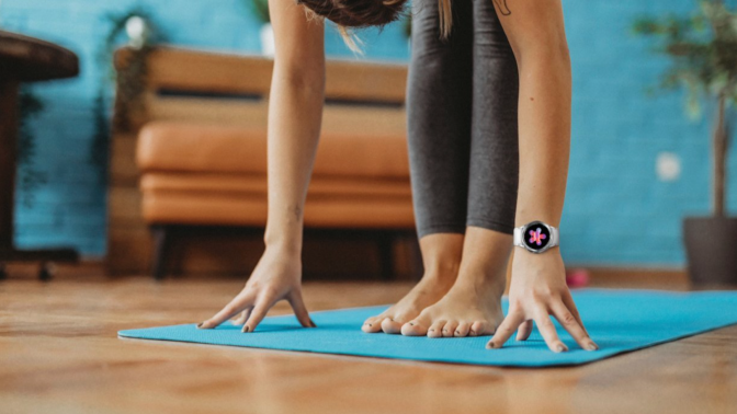hands reaching down on yoga mat with visible smartwatch on left wrist