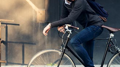 person in dress pants and a sweater riding bike in city setting