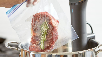 A sous vide machine from Anova Culinary and meat in a kitchen.