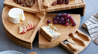 a swiveling cheese board covered in various cheeses and fruits, on a blue backdrop