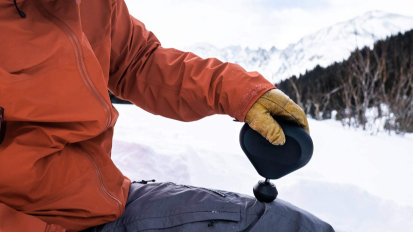 a person using a theragun mini on their upper leg in a snowy environment