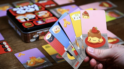 hand holding sushi go party game cards with board in background