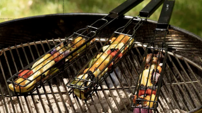 Kabobs in metal baskets on a grill.