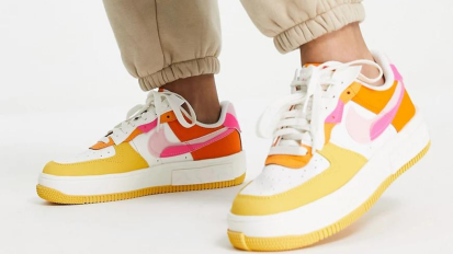 Person's feet wearing white, pink, orange, and yellow Nike sneakers