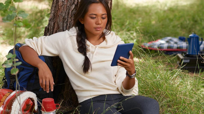Person sitting against a tree and reading a Kindle