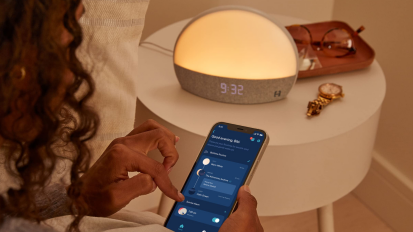 Person using app on phone to control Hatch alarm clock on nightstand