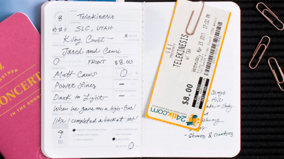 a close-up of a letterfolk concert book containing a ticket stubs next to a closed concert book and a pile of paperclips